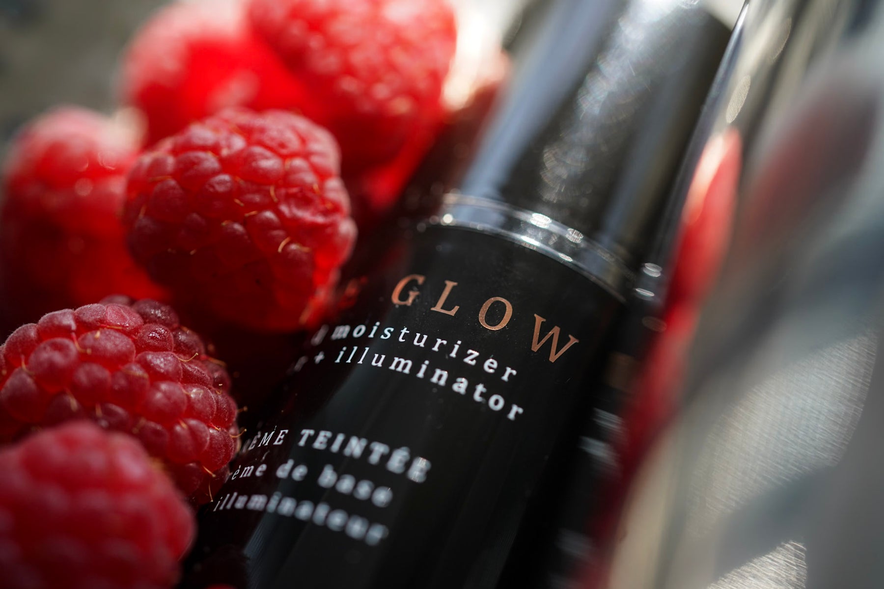 Raspberries in a wooden bowl with an amber glass bottle of raspberry seed oil surrounded by raspberries