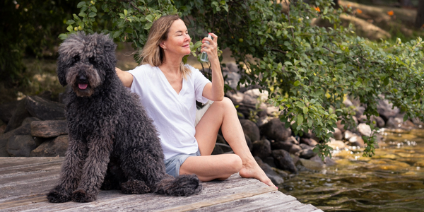 graydon moffat sits on the dock by the lake with a large curly black dog beside her. she is misting face food facial mist on her face, filled with protective and hydrating minerals to quench and soothe the skin