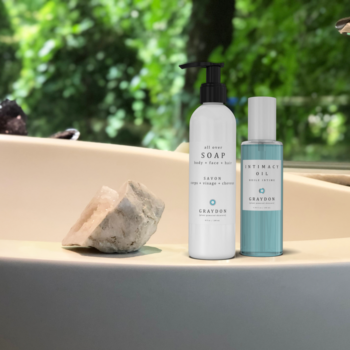 A bottle of vegan soap for sensitive skin next to a bottle of blue-coloured vegan body oil on the ledge of a chic-looking bathtub.