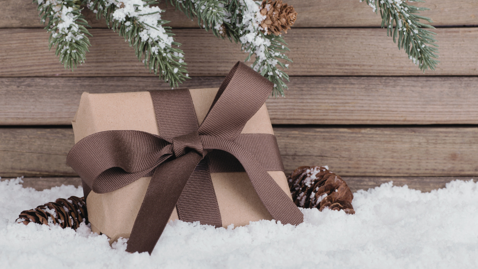 Gift wrapped in brown paper with ribbon sitting in snow.