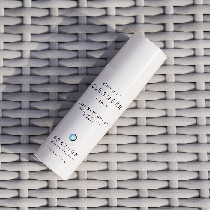 A bottle of soothing milk cleanser for sensitive skin lying on an off-white rattan surface.