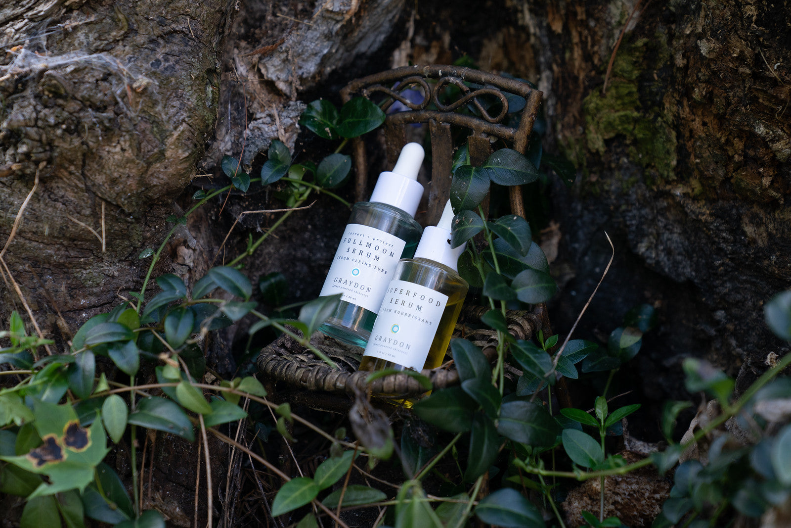 Two serums in glass bottles placed on wooden platform covered with leaves.